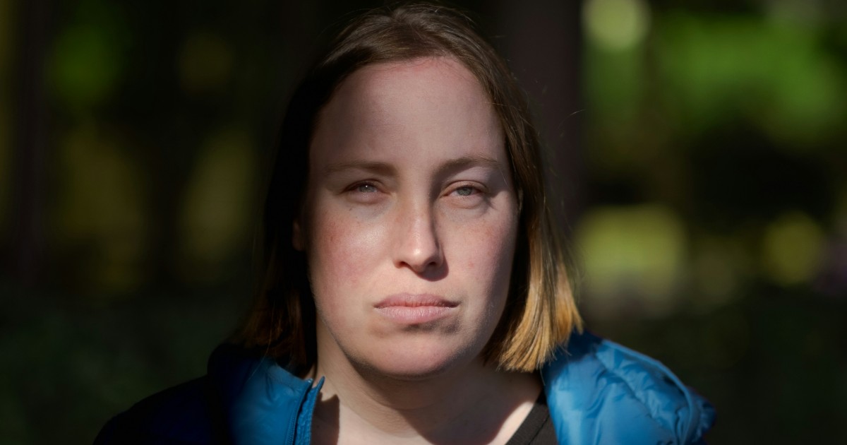 A woman next door wears a blue jacket outside while squinting her eyes with a look of disapproval on her face.