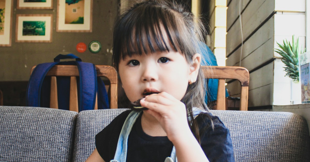 A young girl eats a cookie while sitting on a couch in a cafe