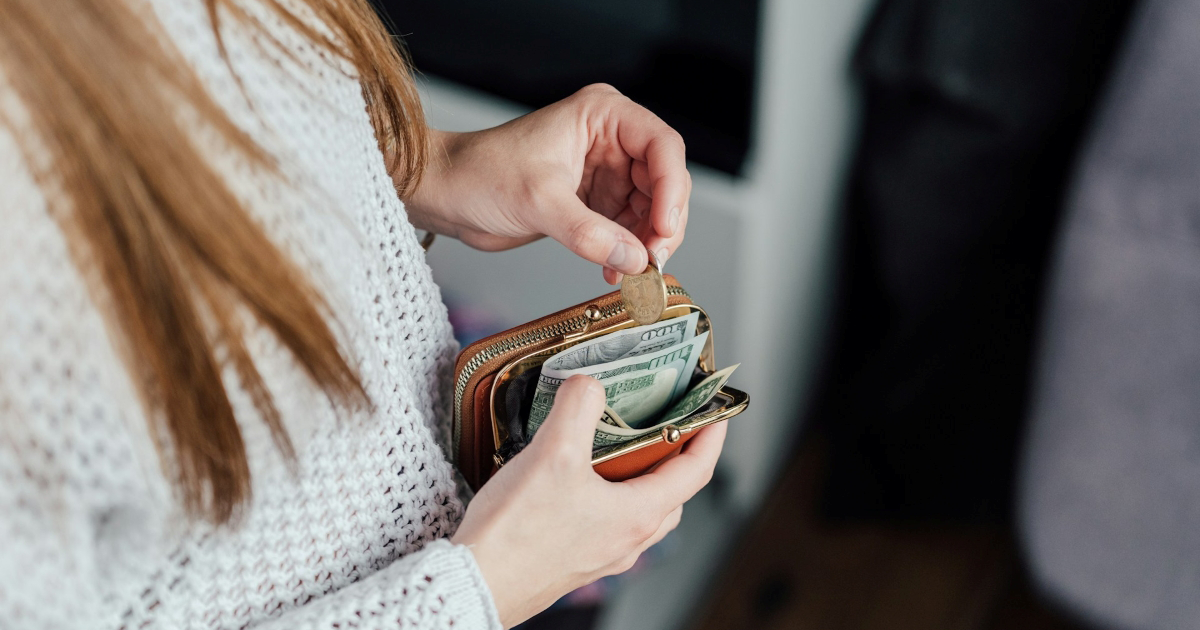 A woman putting a coin in an open wallet with several hundred dollar bills in it