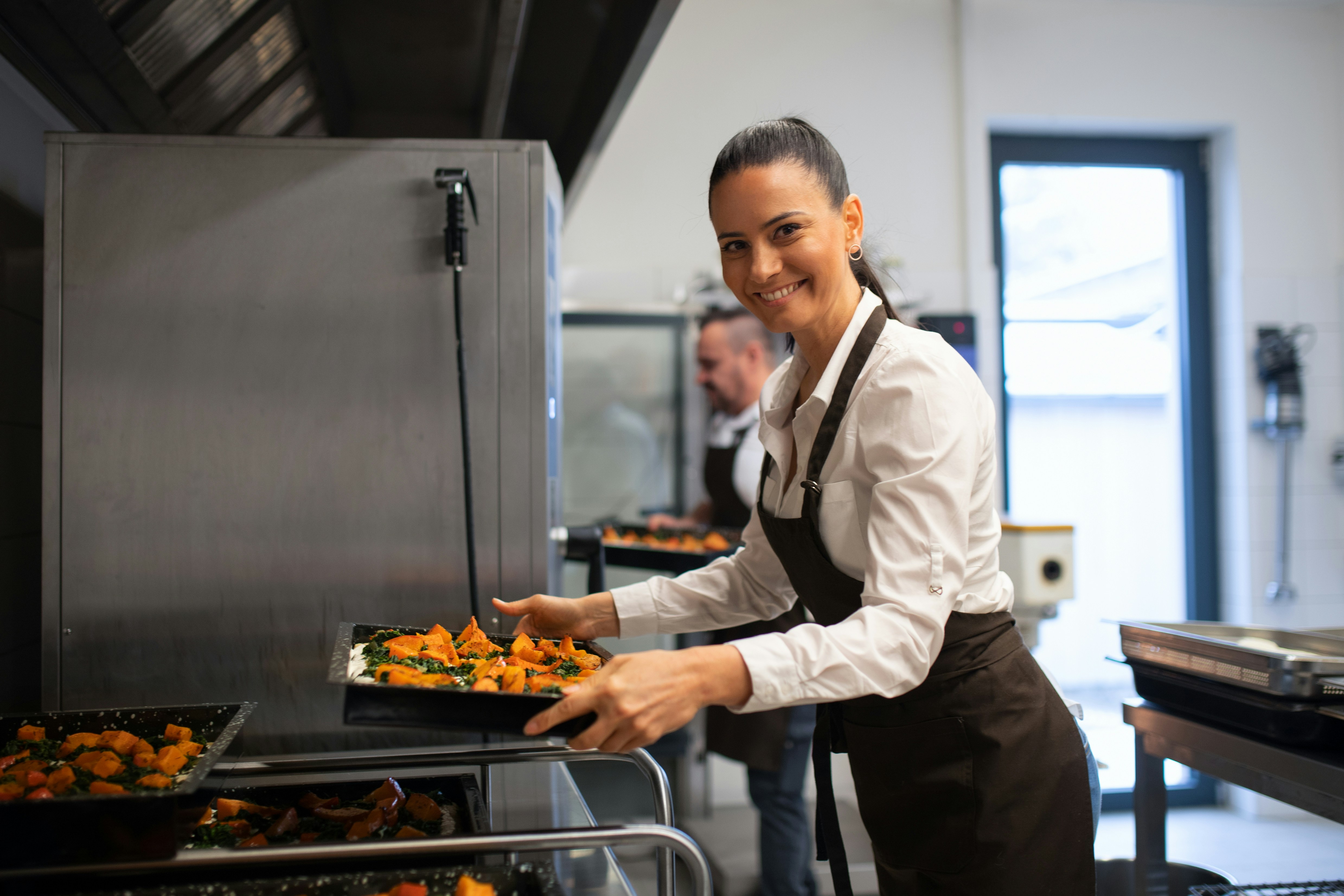 A kitchen worker holds a tray of hot food on a summer day, as depicted by a model.