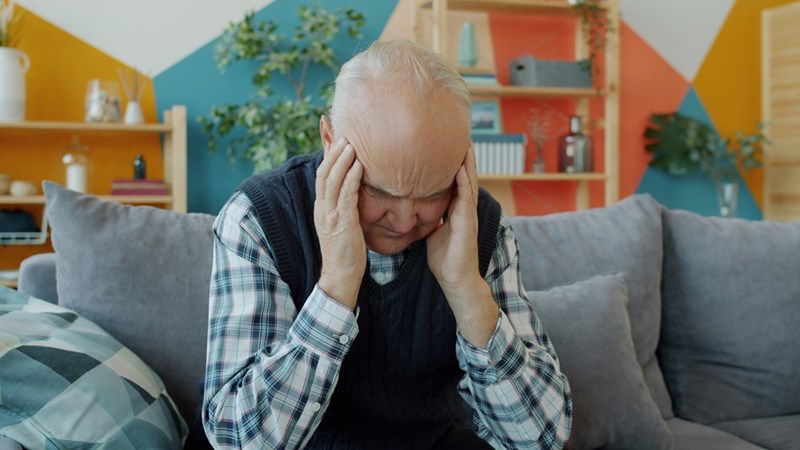 An older man holds his head in discomfort.