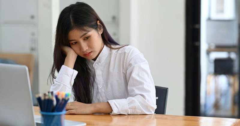 A young female employee rests her head in her hand while sitting at her desk