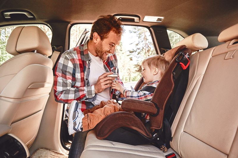 A young father entertains his young child in the backseat of a car.