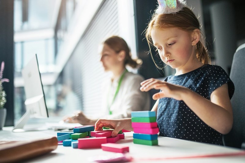 Little girl plays with colorful blocks while her Mom works in the background.