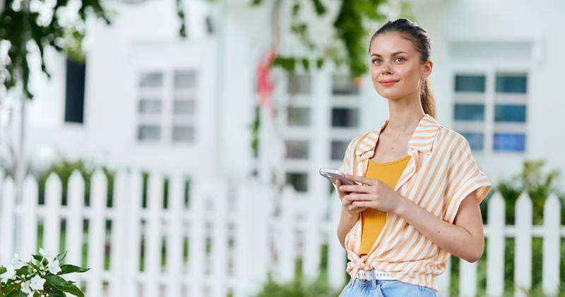 Young woman standing in front of her house watching the street. 