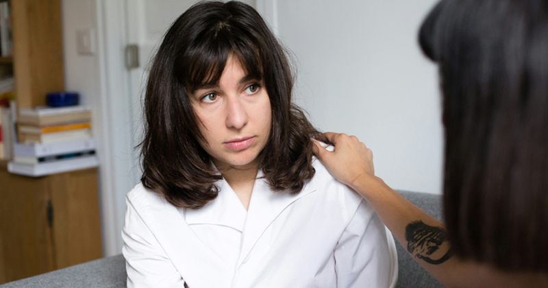 A woman touches the shoulder of another woman as she tells her something