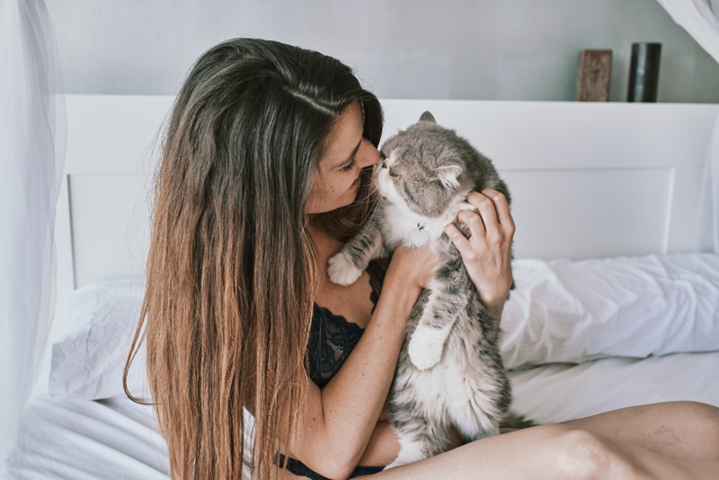 Young woman hugging her cat on bed.