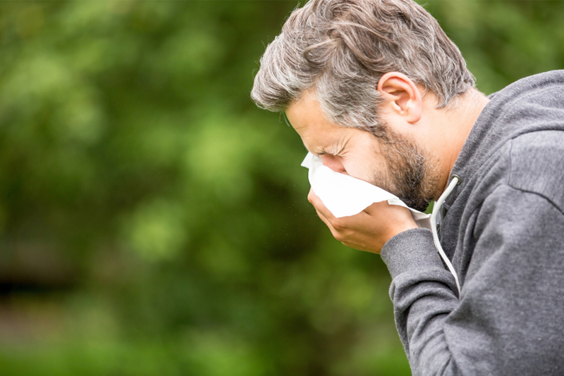 Middle-aged man sneezing into a tissue.