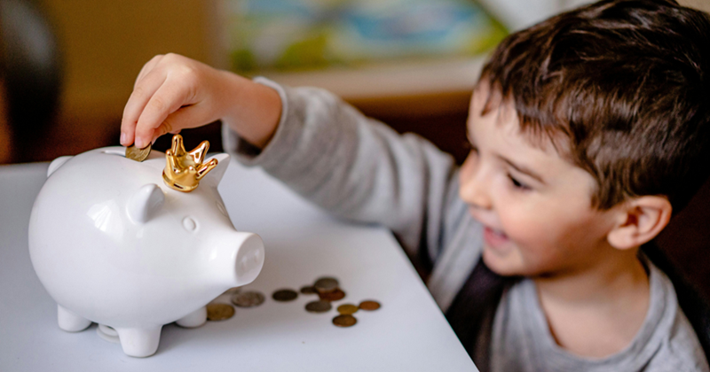Boy in Gray Long Sleeve Shirt Putting Coins in a Piggy Bank