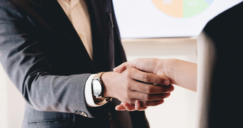 A businessman in a suit shakes hands with another person
