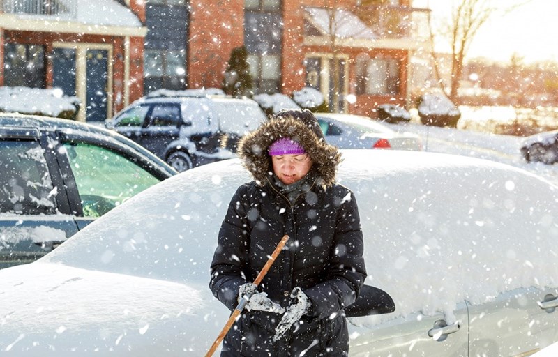 A woman shovels snow in front of her car.
