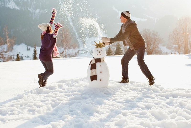 Couple playing in deep snow with a snowman; a contrast to the pressured employee in storm conditions.
