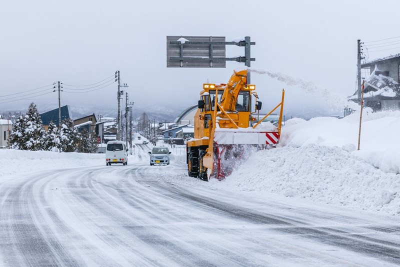 Yellow snow blower clearing a dangerous road for an employee commuting during a heavy winter snowfall.