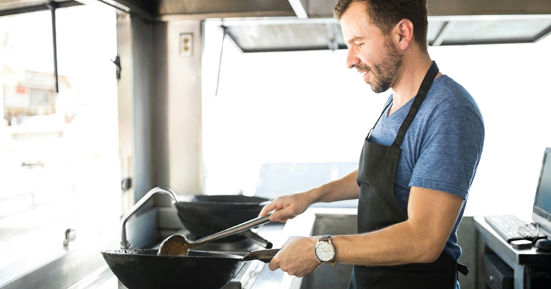 A man heats a pan over an open flame in a food truck