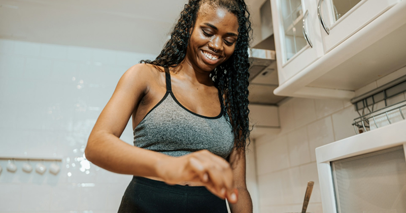 A women wearing athleisure smiles as she prepares something on a kitchen counter