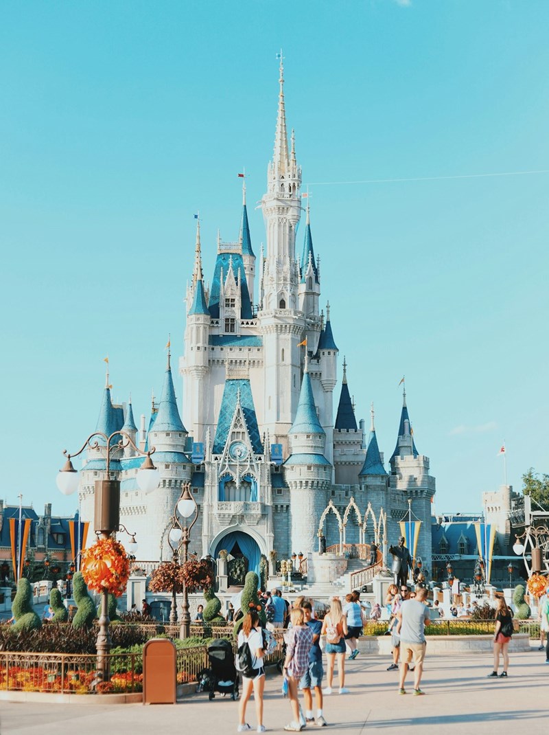 Cinderella Castle at Walt Disney World in Florida, with blue rooftops and white stone towers, surrounded by visitors walking through the theme park on a sunny day.