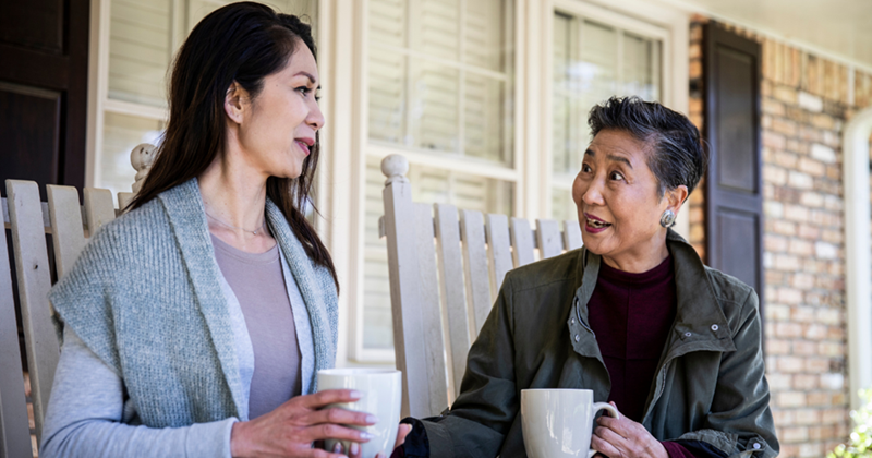 A woman is having tea with her mother on the porch.