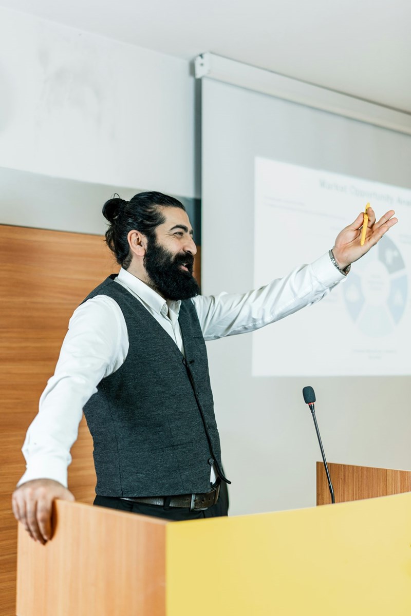 Boss cheerfully invites employee to give his presentation to the other workers.