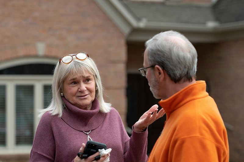 Concerned homeowner discussing property issues with a neighbor outside a brick house.