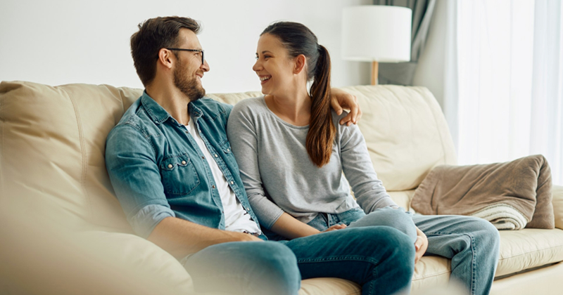A man and a woman look at each other and smile while sitting on a couch