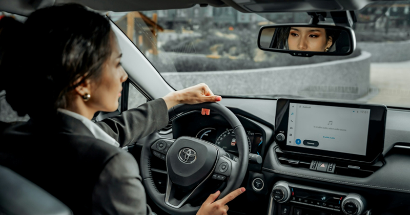 A woman in business attire looks in her windscreen mirror while driving in the city