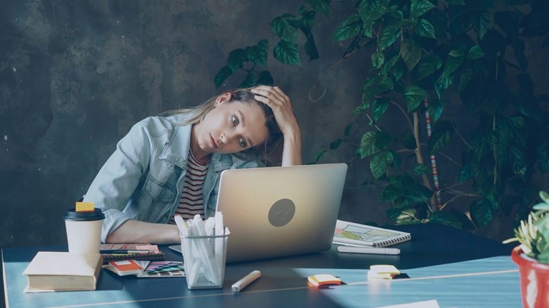 A woman uses her laptop, holding her head out of stress.