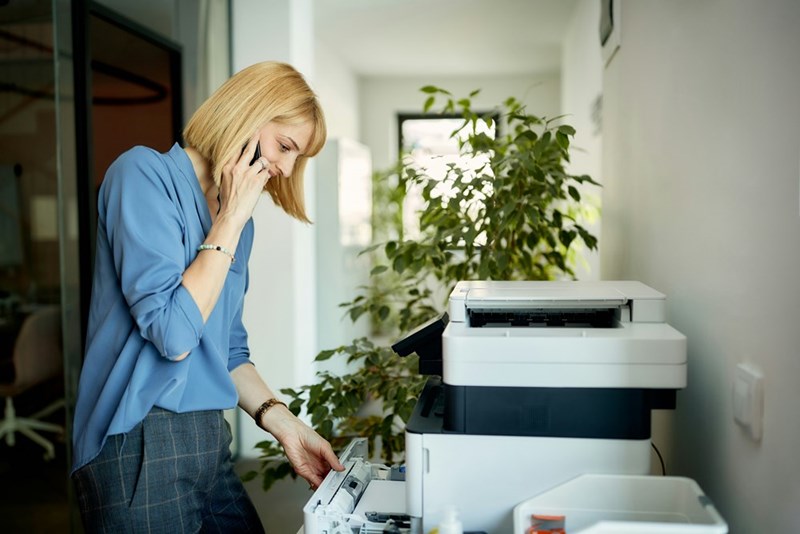 Smiling businesswoman talking on cell phone while using photocopier in the office
