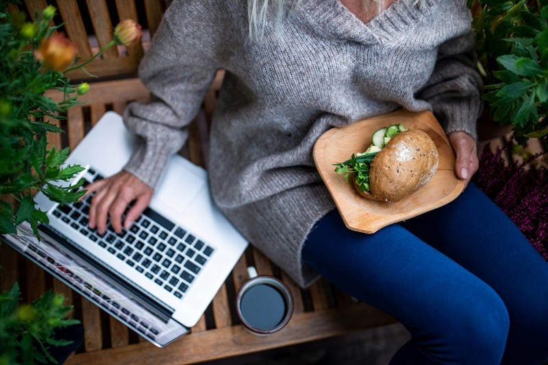 Worker guards lunch from food thief while eating sandwich near laptop. 
