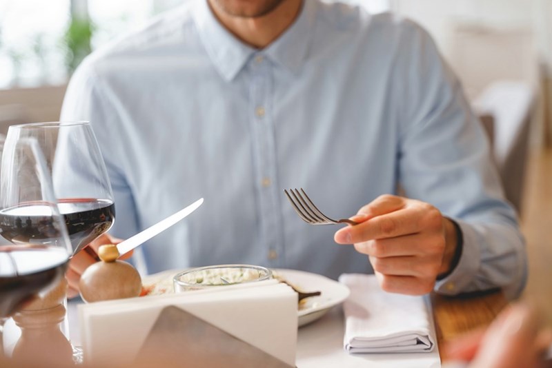 A closeup of male hands holding a fork and a knife at a restaurant