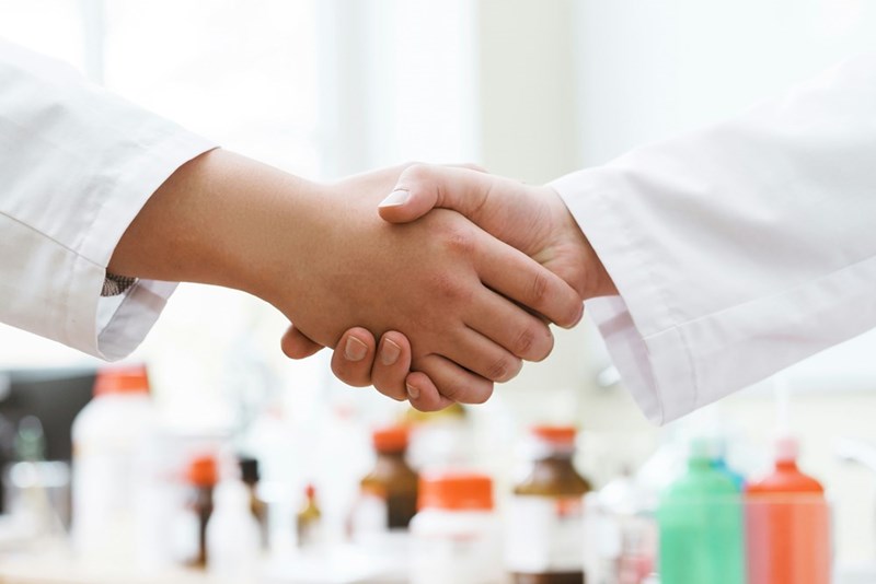 Two people in lab coats shake hands.