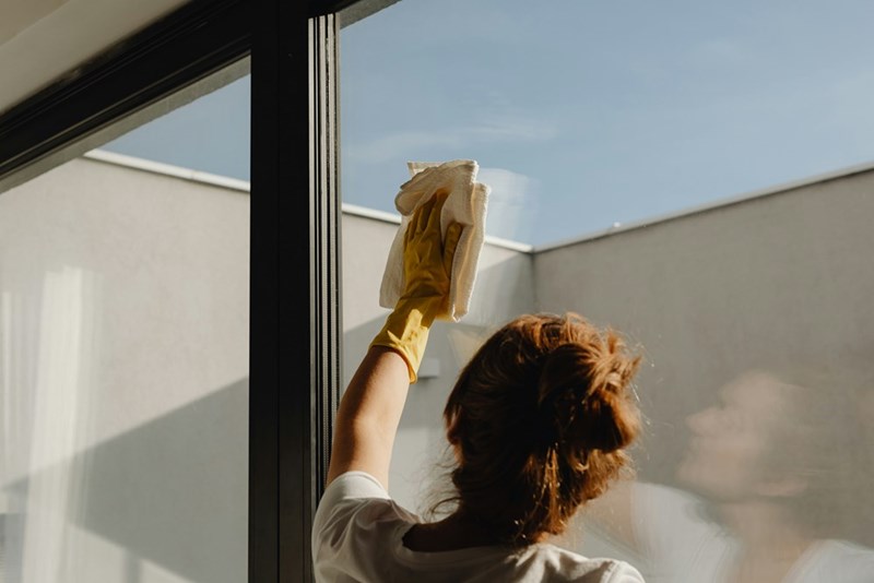 A custodial employee cleans the windows of an establishment.