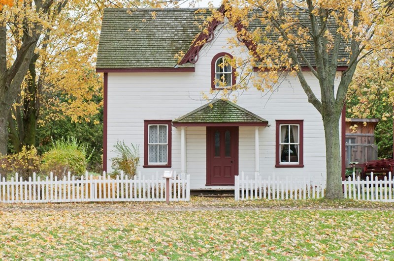 White home with red door and large lawn covered in leaves.