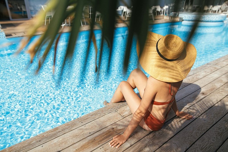 Woman sitting poolside at a summer resort in red swimsuit and large sunhat