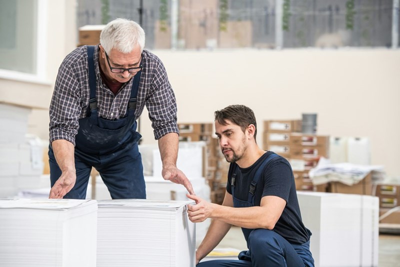 Employee and client inspect large stacks of paper together.