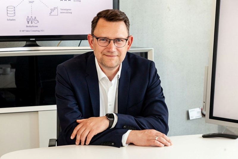 The boss of a small business sits at a desk smiling, even though his business is falling apart