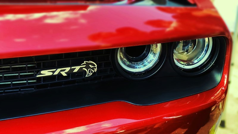 Close-up of the front grille and headlights of a red Dodge Challenger SRT with the SRT Hellcat logo visible on the grille.