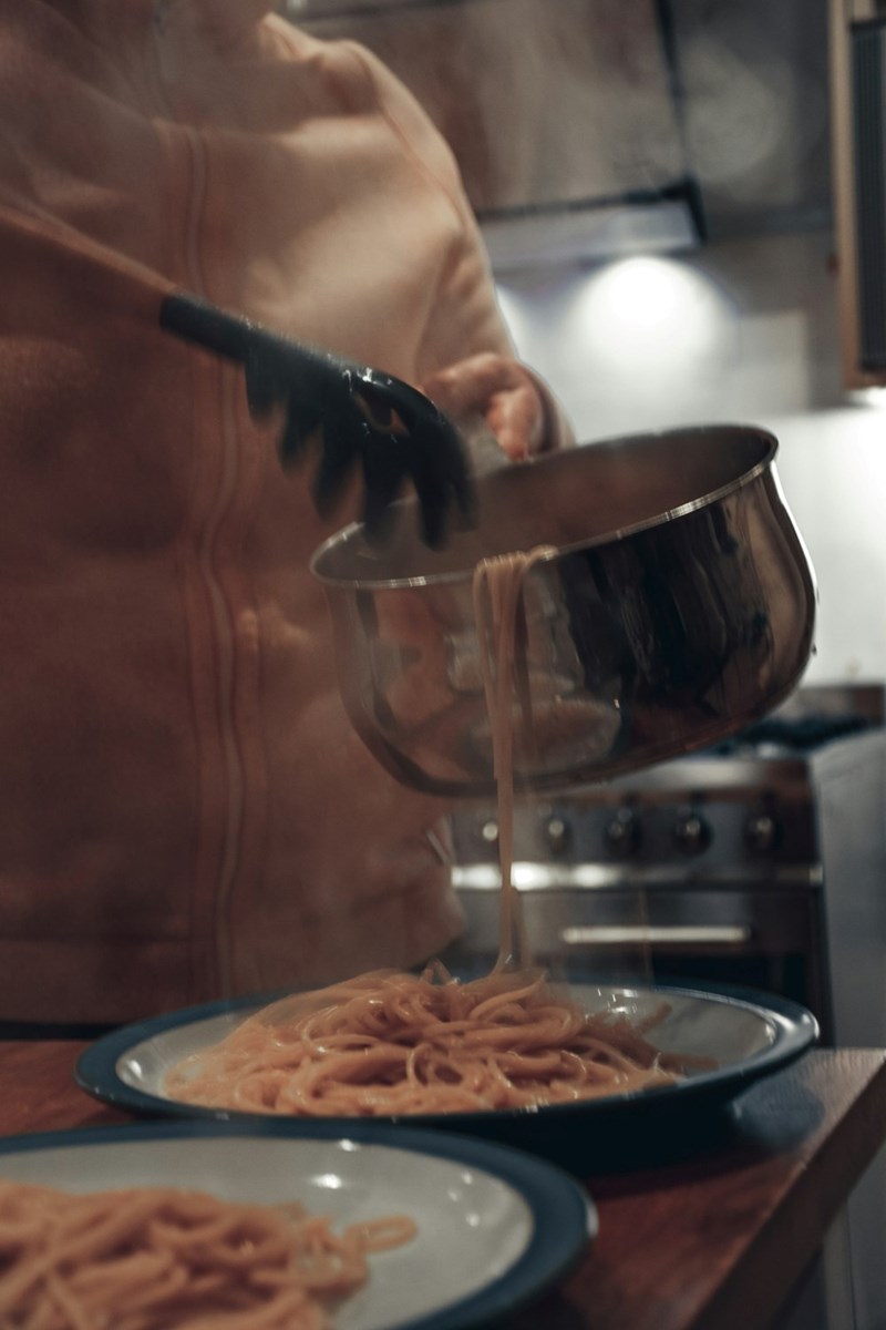 A woman serves pasta onto two plates on a table in the kitchen