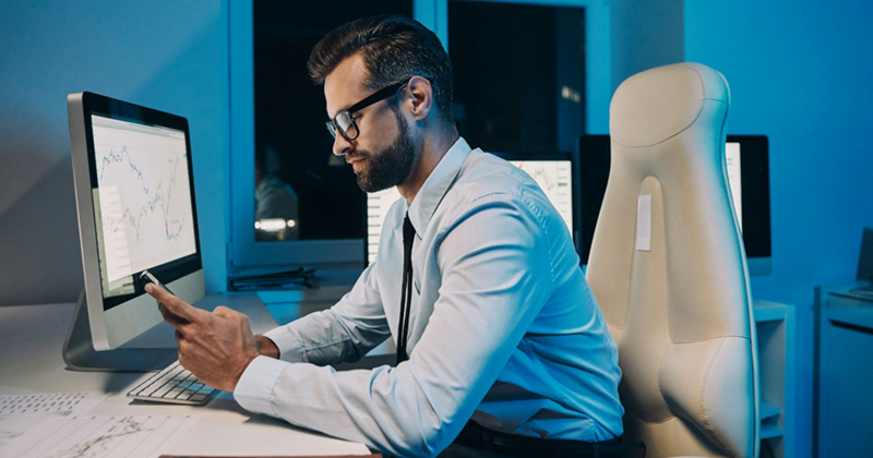 An employee sitting at his computer at night looks at his phone