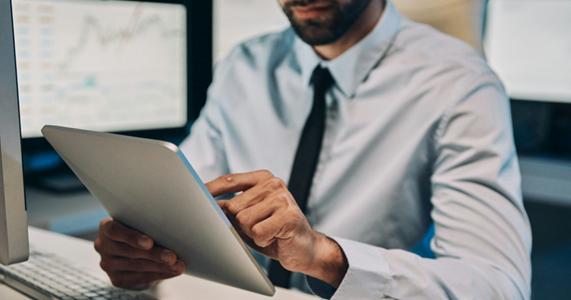 An employee sitting at a computer uses a tablet