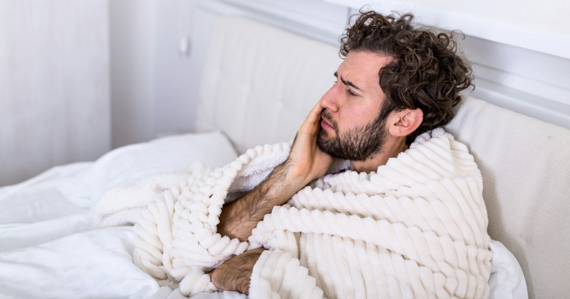 A sick man wrapped in a blanket while sitting in bed