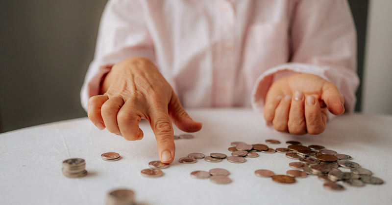 The hands of an older woman counting coins on a table