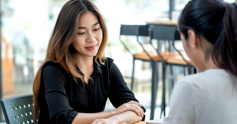 A woman looks down as she is sitting across a table from another woman