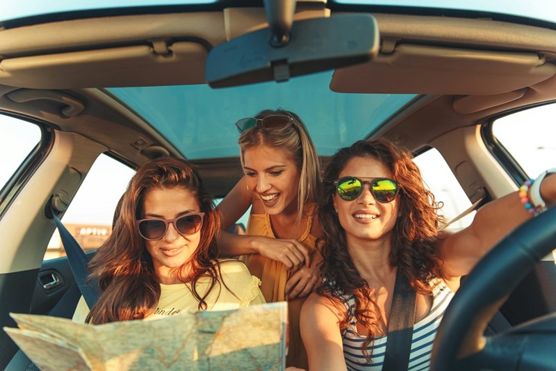 The group of female friends looks at directions while driving down the road.