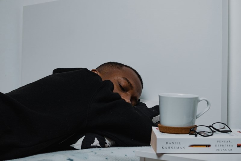 A man sleeping on a bed next to a stack of books