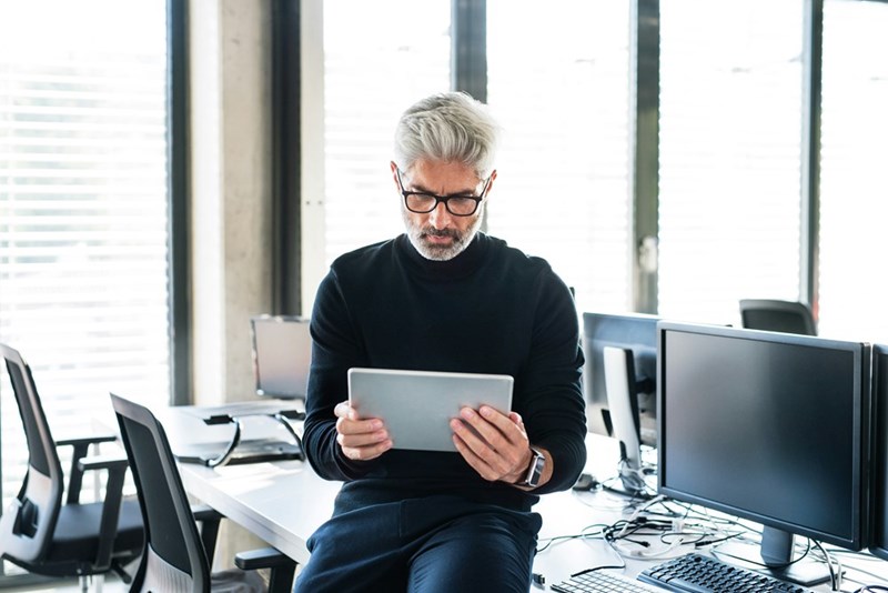 Handsome mature businessman with tablet sitting on a desk in the office