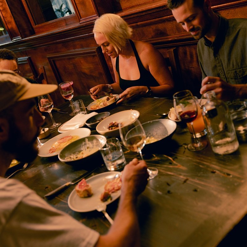 A group of friends sits around the dinner table, sharing food.