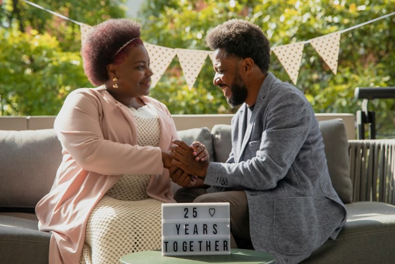 A man and a woman sitting on a couch holding hands during their 25th anniversary