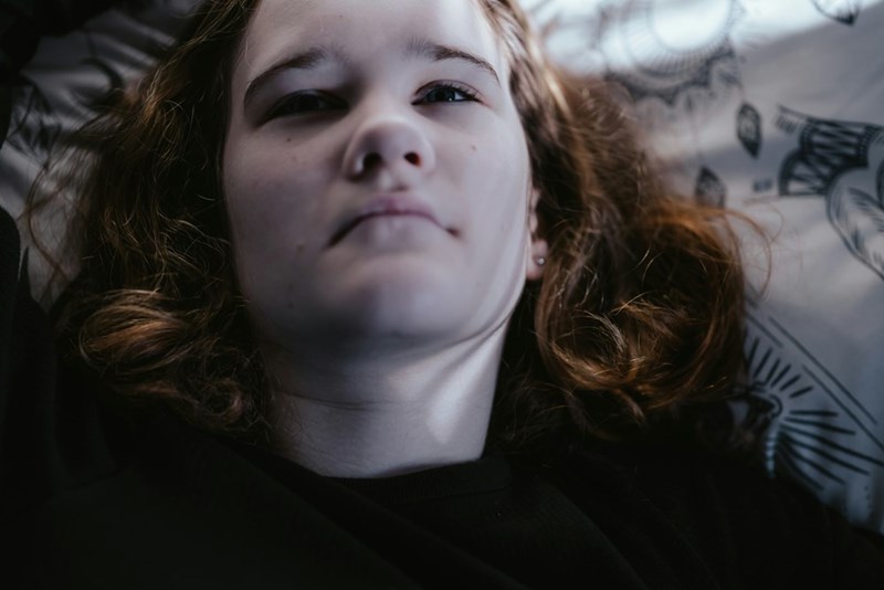 A close-up of a teen girl's face as she sits alone, lying down on a couch.