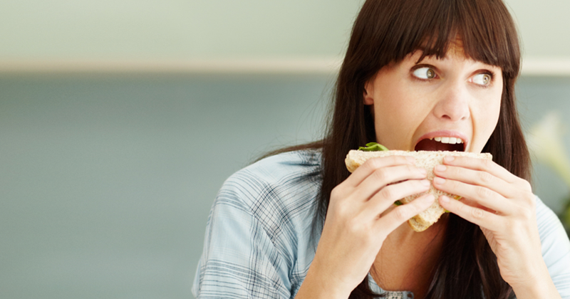Woman secretly eating a sandwich on her lunch break. 
