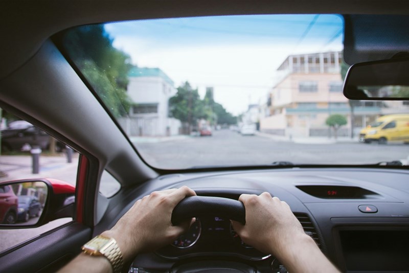 Two hands driving a car, street from the driver's perspective